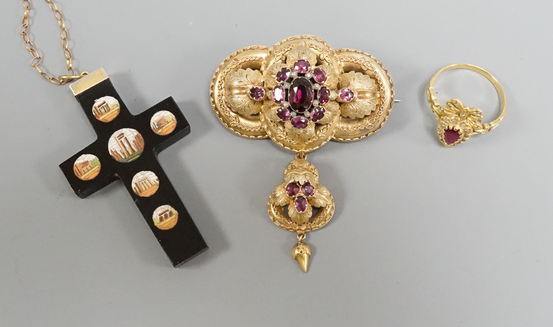 A Victorian yellow metal and garnet cluster set drop brooch, 50mm, a modern 18ct gold, ruby and diamond heart shaped ring with ribbon bow crest and a micro mosaic set cross pendant, on a 9k chain.